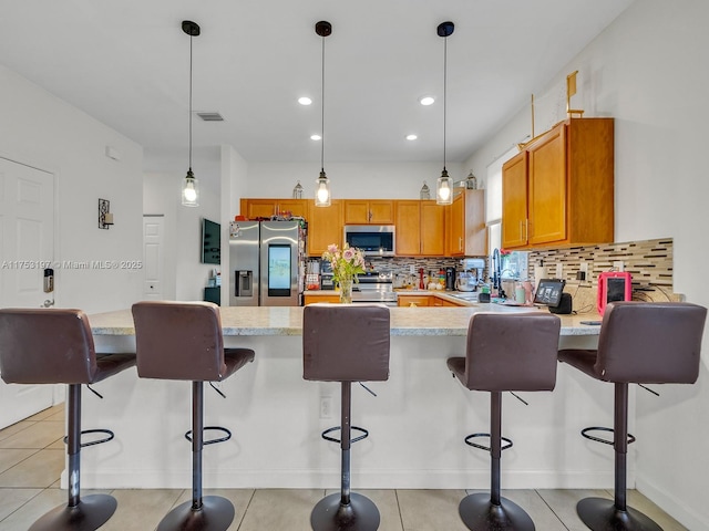 kitchen featuring stainless steel appliances, visible vents, decorative backsplash, brown cabinetry, and decorative light fixtures