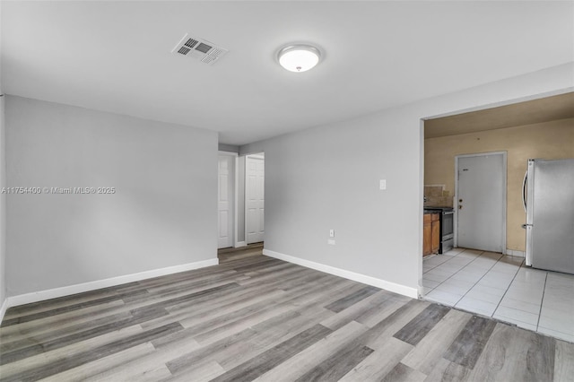 unfurnished room with light wood-type flooring, visible vents, and baseboards