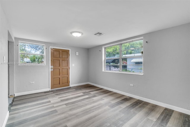 unfurnished room featuring a healthy amount of sunlight, baseboards, visible vents, and wood finished floors