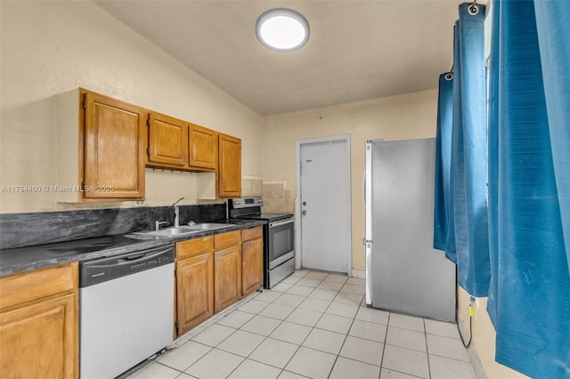 kitchen with dark countertops, brown cabinets, stainless steel appliances, a sink, and light tile patterned flooring