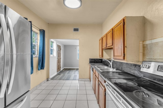 kitchen featuring light tile patterned flooring, stainless steel appliances, a sink, visible vents, and brown cabinetry