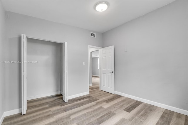 unfurnished bedroom featuring a closet, visible vents, baseboards, and wood finished floors