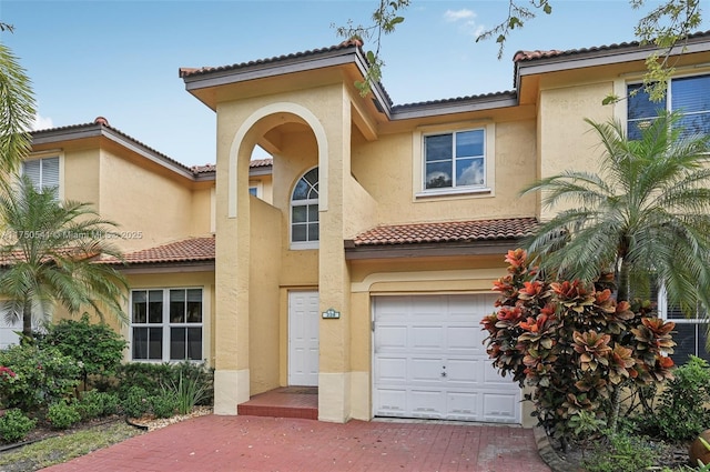 mediterranean / spanish-style home with a garage, a tile roof, decorative driveway, and stucco siding