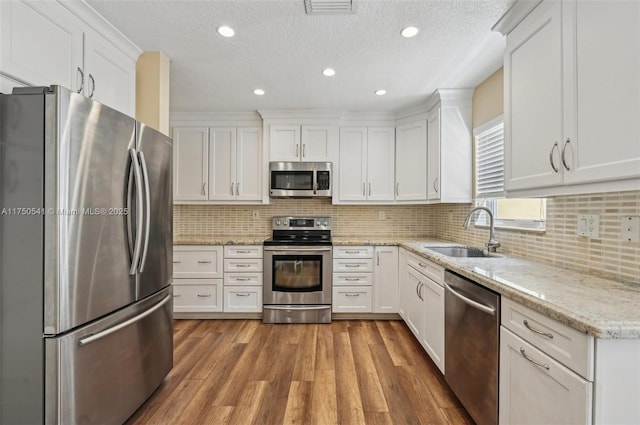 kitchen with visible vents, appliances with stainless steel finishes, white cabinetry, a sink, and wood finished floors