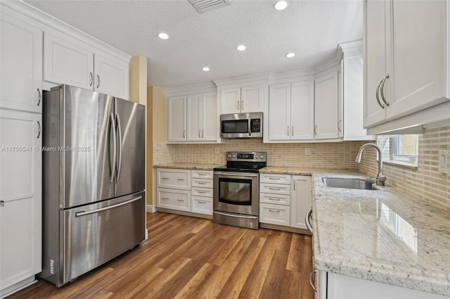 kitchen featuring visible vents, appliances with stainless steel finishes, white cabinetry, a sink, and wood finished floors