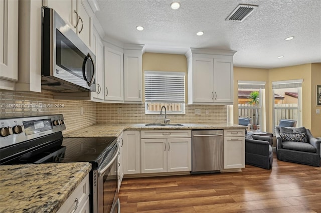 kitchen with visible vents, white cabinets, appliances with stainless steel finishes, wood finished floors, and a sink