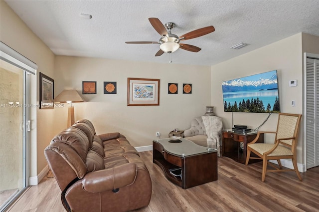 living area featuring baseboards, visible vents, a ceiling fan, wood finished floors, and a textured ceiling