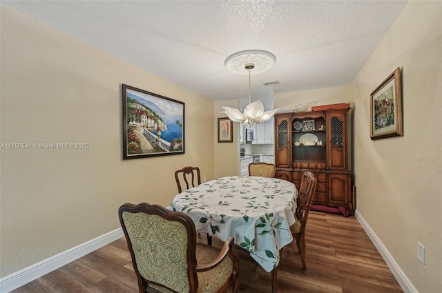 dining space featuring a textured ceiling, visible vents, baseboards, dark wood finished floors, and an inviting chandelier