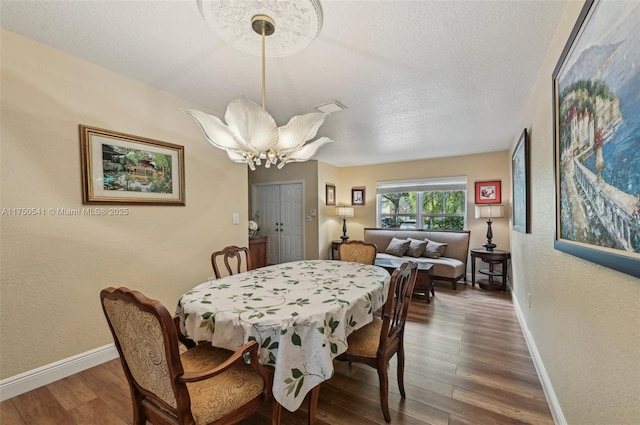 dining area with an inviting chandelier, a textured ceiling, baseboards, and wood finished floors