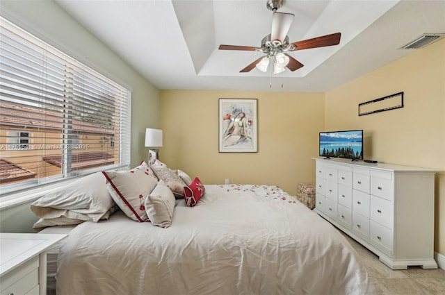 bedroom with a tray ceiling, visible vents, and ceiling fan