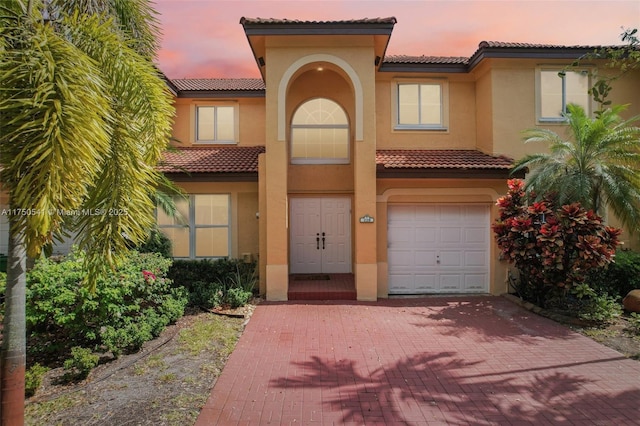 mediterranean / spanish-style home with a garage, a tiled roof, decorative driveway, and stucco siding