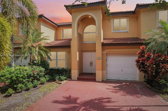 mediterranean / spanish house with decorative driveway, a tiled roof, an attached garage, and stucco siding