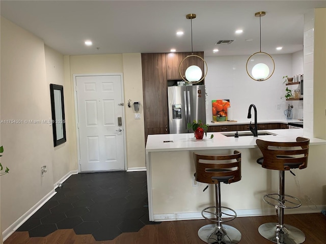 kitchen featuring visible vents, light countertops, a kitchen bar, stainless steel refrigerator with ice dispenser, and a sink