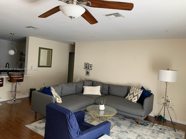 living area featuring a ceiling fan, visible vents, baseboards, and wood finished floors