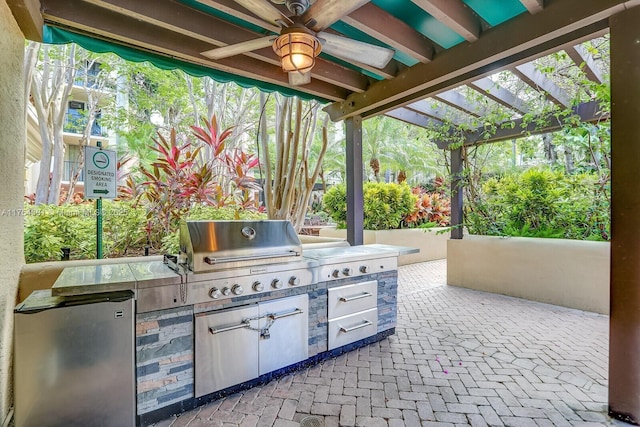 view of patio / terrace featuring area for grilling, an outdoor kitchen, a ceiling fan, and a pergola