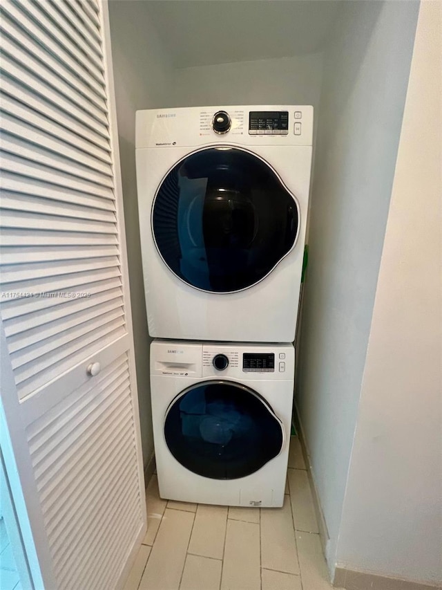 laundry room featuring laundry area, baseboards, tile patterned floors, and stacked washing maching and dryer