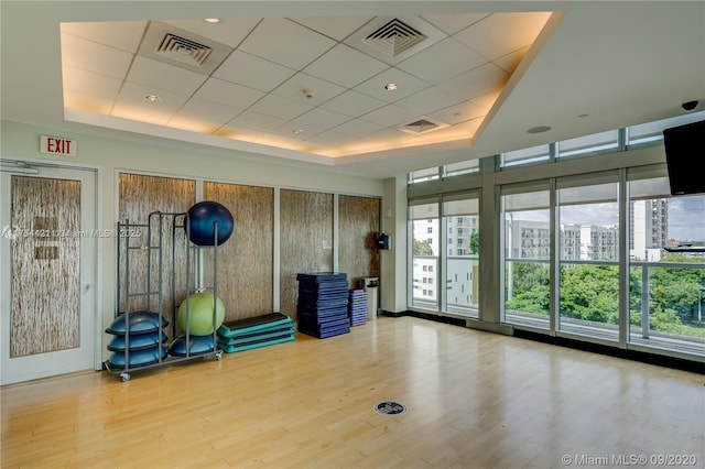 exercise room featuring visible vents, plenty of natural light, a raised ceiling, and wood finished floors