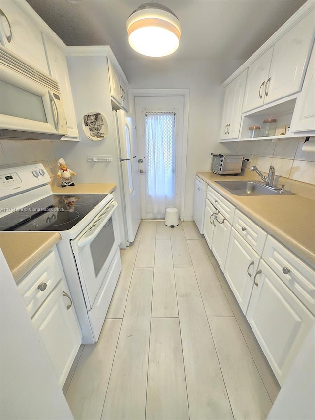 kitchen featuring white appliances, decorative backsplash, light countertops, white cabinetry, and a sink