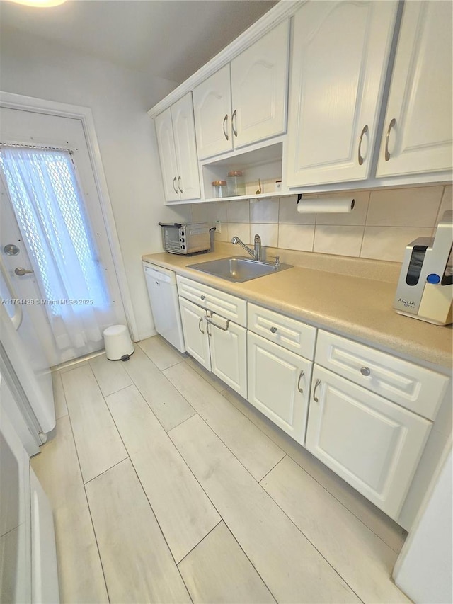 kitchen with tasteful backsplash, light countertops, white cabinets, a sink, and dishwasher