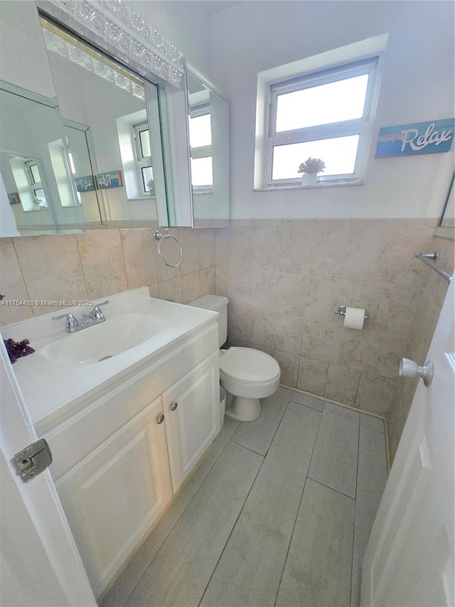 half bathroom with toilet, a wainscoted wall, tile walls, and vanity