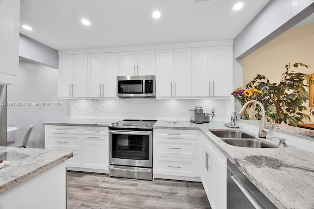 kitchen with light stone counters, a sink, light wood-style floors, appliances with stainless steel finishes, and backsplash