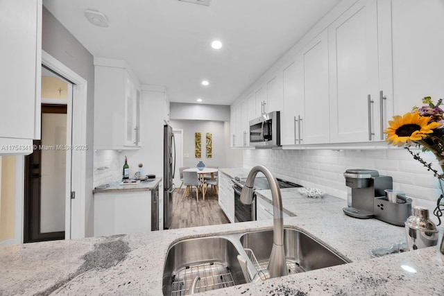 kitchen featuring a sink, light stone countertops, stainless steel appliances, white cabinetry, and backsplash