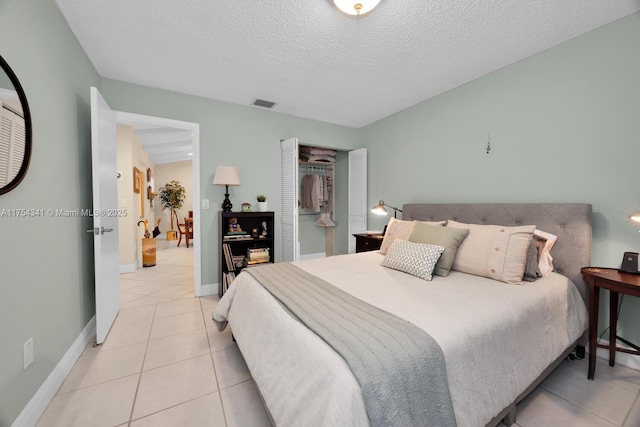 bedroom with a textured ceiling, light tile patterned flooring, visible vents, baseboards, and a closet