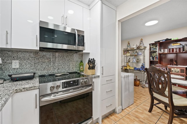 kitchen with light stone countertops, white cabinetry, stainless steel appliances, and backsplash