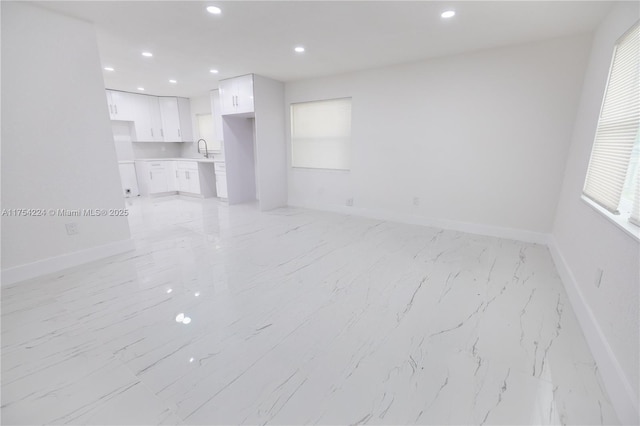 unfurnished living room featuring baseboards, a sink, and recessed lighting