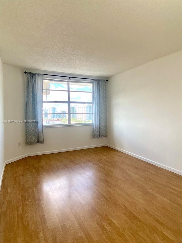 spare room featuring a textured ceiling, baseboards, and wood finished floors