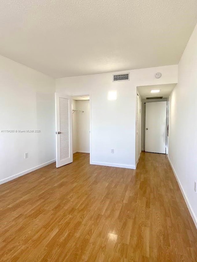 empty room featuring light wood-style floors, baseboards, visible vents, and a textured ceiling