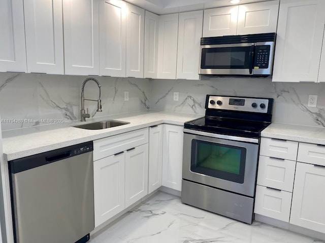 kitchen with a sink, marble finish floor, stainless steel appliances, white cabinetry, and backsplash