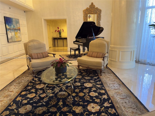 living area with ornate columns, a decorative wall, and tile patterned floors