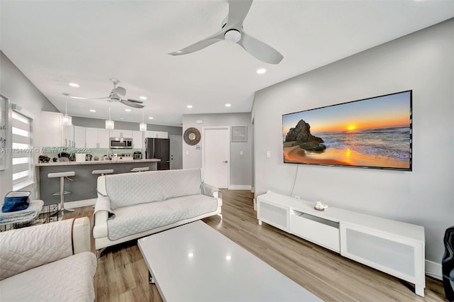 living room featuring baseboards, light wood-type flooring, a ceiling fan, and recessed lighting