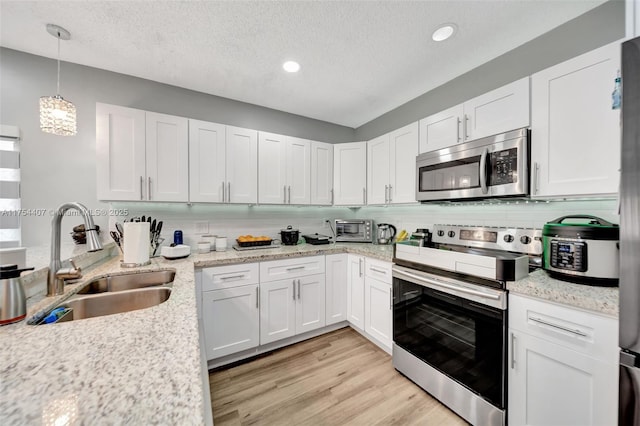 kitchen featuring light wood finished floors, tasteful backsplash, appliances with stainless steel finishes, white cabinetry, and a sink