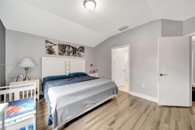 bedroom featuring visible vents, light wood-style floors, vaulted ceiling, a textured ceiling, and baseboards