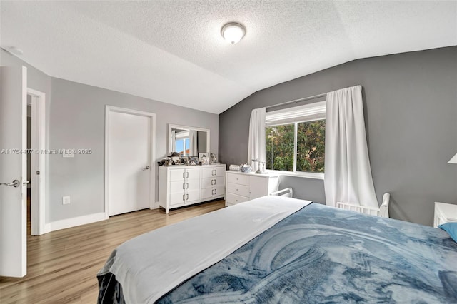 bedroom featuring lofted ceiling, a textured ceiling, light wood-type flooring, and baseboards