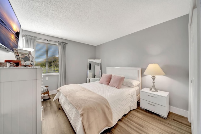 bedroom featuring a textured ceiling, light wood finished floors, and baseboards