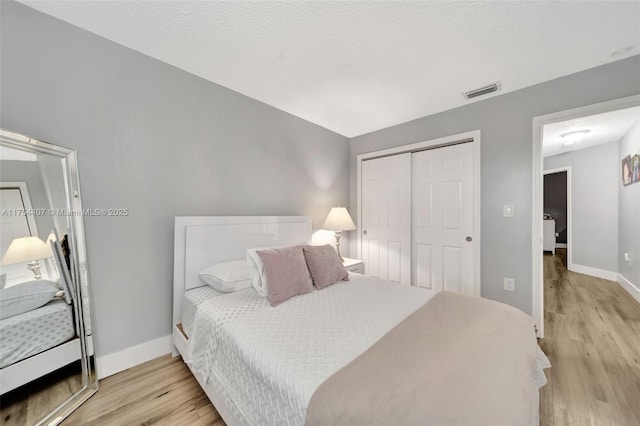 bedroom with a textured ceiling, light wood-style flooring, visible vents, baseboards, and a closet