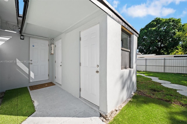 doorway to property with a yard, fence, and stucco siding