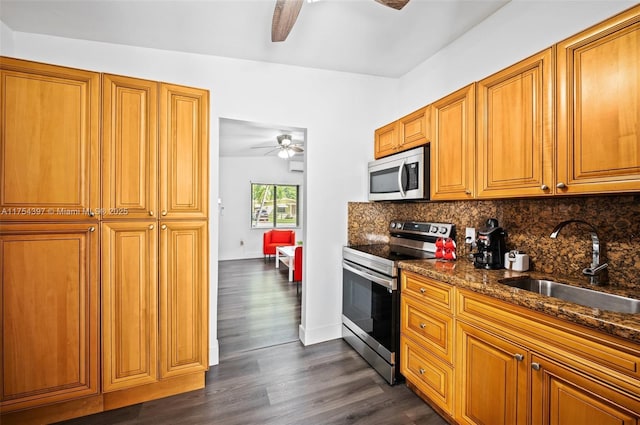 kitchen with a ceiling fan, appliances with stainless steel finishes, dark wood-type flooring, a sink, and backsplash