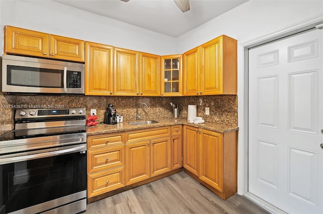 kitchen featuring light wood finished floors, glass insert cabinets, appliances with stainless steel finishes, a sink, and backsplash