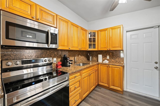 kitchen featuring tasteful backsplash, light wood-style flooring, appliances with stainless steel finishes, stone countertops, and a sink