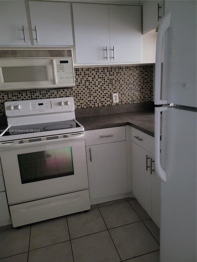 kitchen with light tile patterned floors, dark countertops, backsplash, white cabinetry, and white appliances