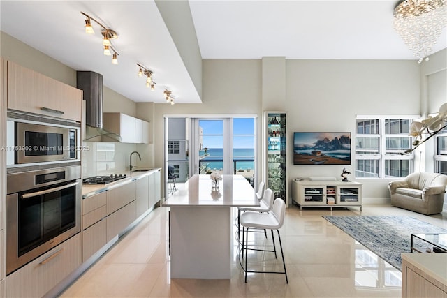 kitchen featuring a breakfast bar, light tile patterned floors, stainless steel appliances, a sink, and wall chimney exhaust hood