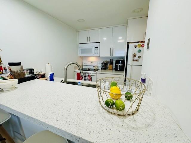 kitchen with a peninsula, white appliances, a breakfast bar, a sink, and light countertops