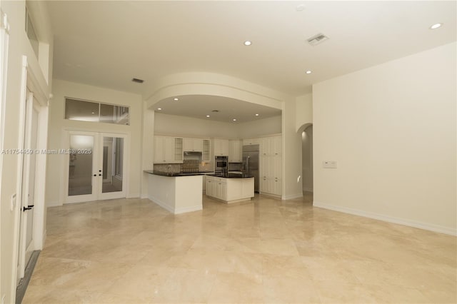 kitchen with arched walkways, dark countertops, appliances with stainless steel finishes, open floor plan, and white cabinets