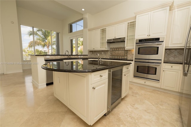 kitchen featuring an island with sink, wine cooler, appliances with stainless steel finishes, backsplash, and a sink