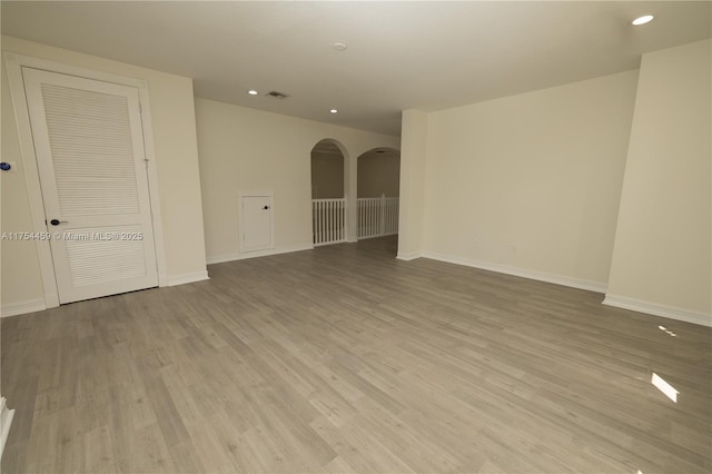 unfurnished room featuring arched walkways, recessed lighting, wood finished floors, visible vents, and baseboards