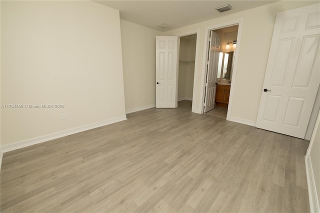 unfurnished bedroom featuring baseboards, visible vents, a spacious closet, light wood-type flooring, and a closet